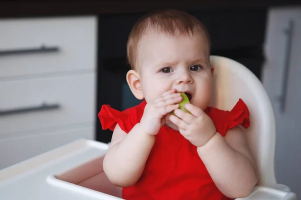 Baby i en röd klänning sitter på en barnstol — Stockfoto