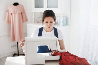 Bir dikiş makinesi üzerinde mavi bir elbise içinde çok sevimli genç kız diker.