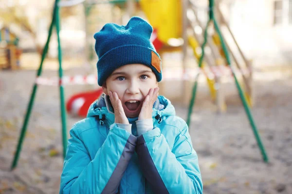 Una linda adolescente con una chaqueta azul y un sombrero verde, dio un grito sorprendido, presionando sus manos en su cara — Foto de Stock