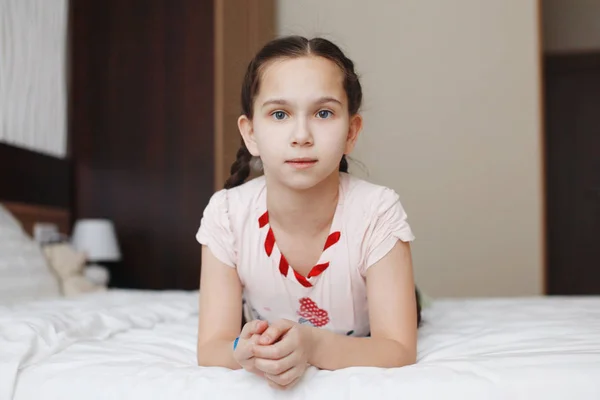 Schattige tiener meisje ligt op bed met witte kleren en kijkt naar de camera — Stockfoto