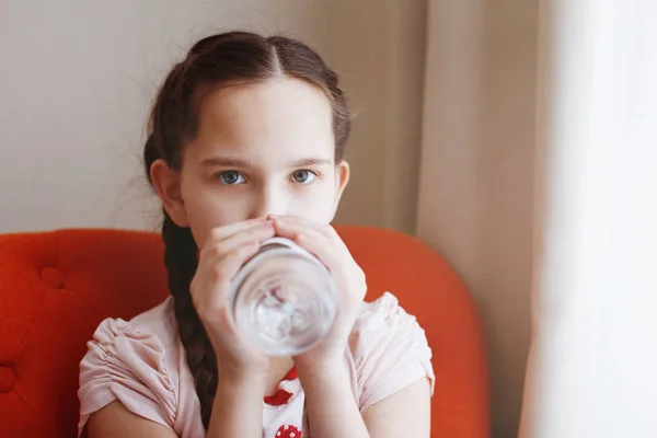 Een jong mooi meisje met vlechten dranken water uit een fles. — Stockfoto