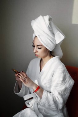 Bir duş bir havlu ile sarılmış bir smartphone ile pencere yakın bir sandalyede oturuyor sonra bir genç kız