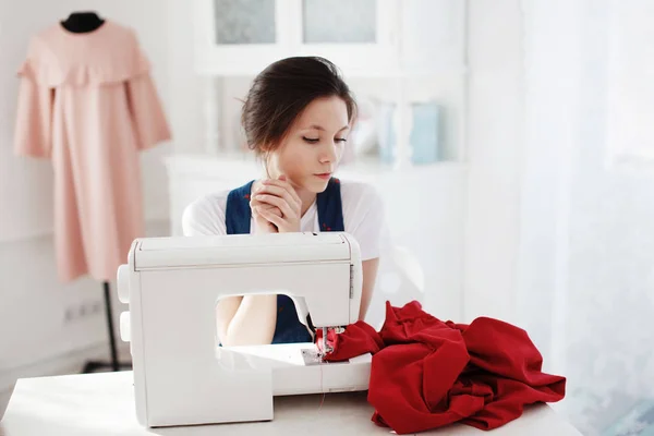 Симпатична молода дівчина в блакитній сукні шиє на швейній машинці . — стокове фото