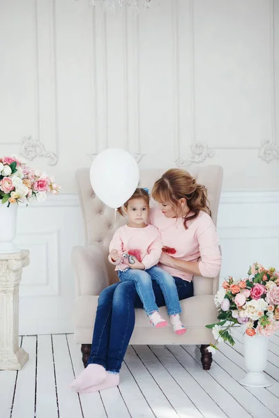 Anne ve kızı pembe bir koltukta oturuyor. Bunun yanında vazolar çiçek, anne ve çocuk gülümseyen ve kameraya bakarak vardır — Stok fotoğraf