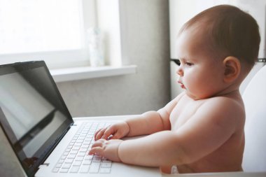 Bebek bir dizüstü bilgisayar ile beyaz bir sandalyesi oturur