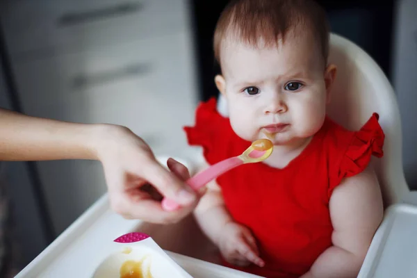 Baby i en röd klänning sitter på en barnstol — Stockfoto