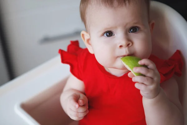 Baby i en röd klänning sitter på en barnstol — Stockfoto