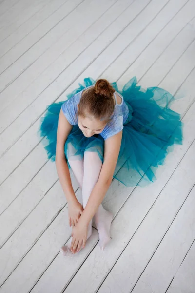 Pembe pointes ile mavi bir etekle genç balerin bir beyaz tahta bankta oturur. — Stok fotoğraf