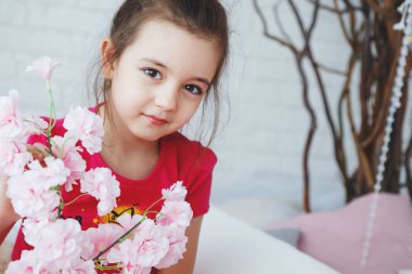 Pembe bir T-shirt ve şort ve golf uzun saçlı bir kız ile bir buket çiçek ile bir ağacın yatakta oturur