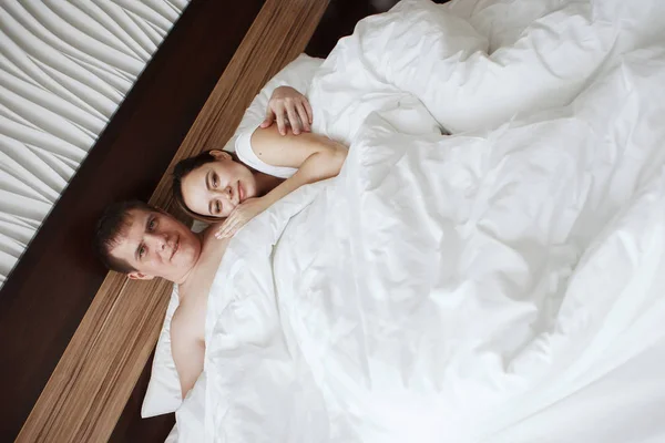 Jonge mooie man en vrouw rusten in bed onder een witte deken in een hotelkamer — Stockfoto