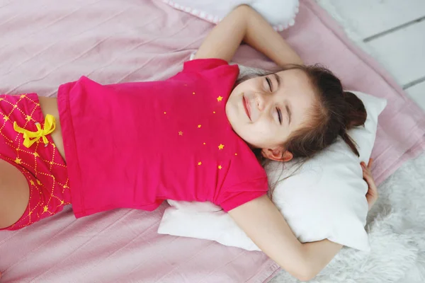 Uzun saçlı kız pembe bir T-shirt ve şort yastık ile yatakta yatıyor. — Stok fotoğraf