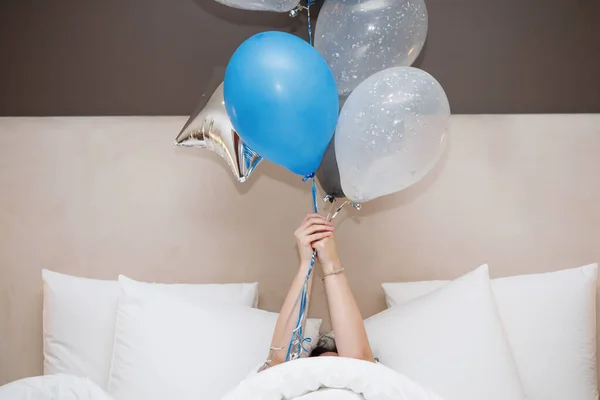 Jonge vrouw met ballonnen ligt in bed. — Stockfoto