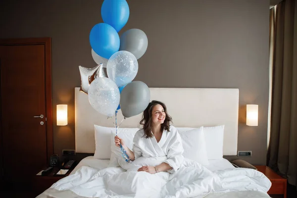 拿着气球的年轻女人躺在床上. — 图库照片