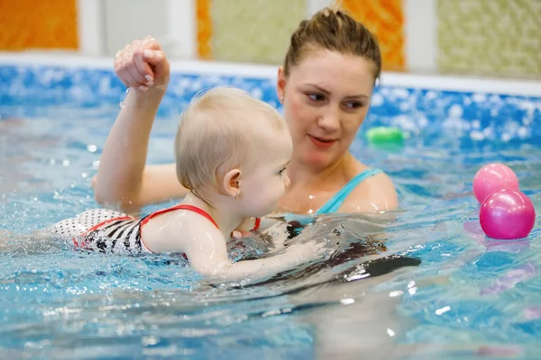 Woman child trainer and toddler swim and study in blue water pool