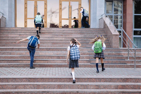 Group of schoolchildren in uniform with backpacks run down the steps to school.