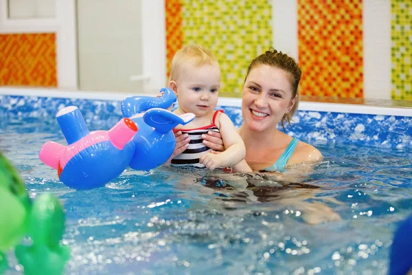 Woman child trainer and toddler swim and study in blue water pool