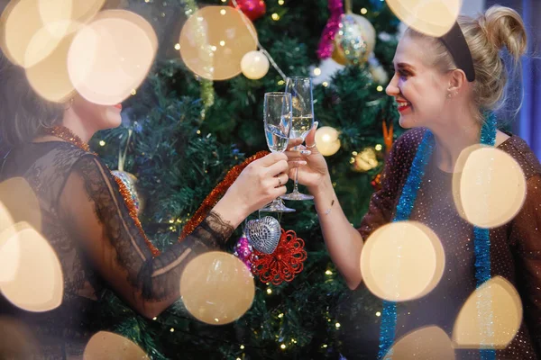 美丽的女人在圣诞树旁喝着一杯香槟玩乐 女人笑 摆姿势 特殊的老式噪音和颗粒过滤器 模糊灯 — 图库照片