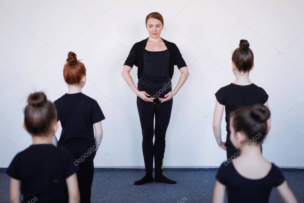 Group of teenage girls dancers in a lesson with a trainer. Black leotard, hair in a bun, white socks.