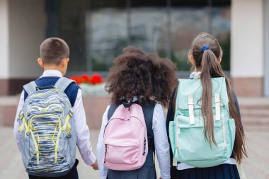 Üniformalı ve sırt çantalı öğrenciler okula gider..