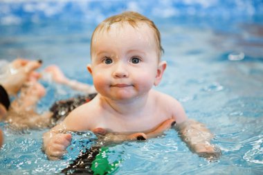 Tatlı bebek havuzda yüzmeyi bir eğitmenin yardımıyla öğreniyor..