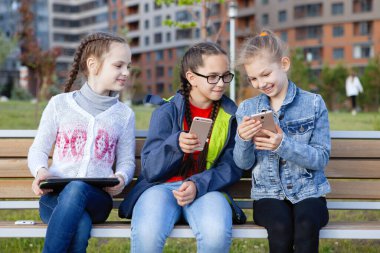 Akıllı telefonlu üç genç kız bir yaz parkında bankta oturuyor..