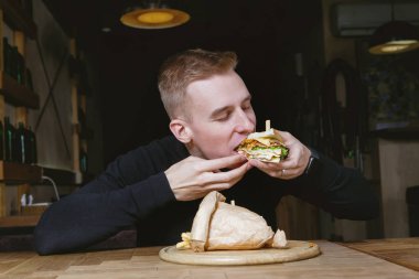 Genç yakışıklı sarışın adam bir kafede sandviç yiyor..
