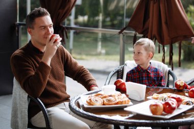 Father and son are sitting at a table in a cafe. Parental love, happy childhood, child care.