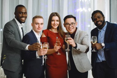 Bir grup çok ırklı insan ellerinde şarap kadehleriyle tatilde ayakta duruyor..