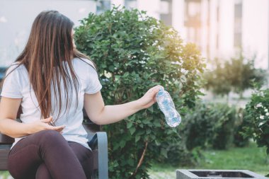 Çöp tenekesinin yanındaki kadın plastik şişe fırlatıyor. Çevresel okuma yazma, doğayla ilgilenme, ayrı çöp toplama..