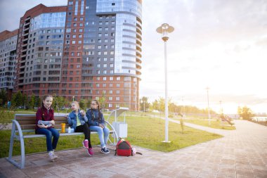Genç kızlar şehir parkında bir bankta yemek yerler. Sağlıklı yemek, beslenme çantası. İnsanlar, çocuklar, arkadaşlar ve arkadaşlık kavramı.