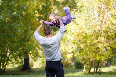 Baba ve kızı yaz parkında eğleniyor. Bir adam bir kızı havada döndürür, el ele tutuşur..