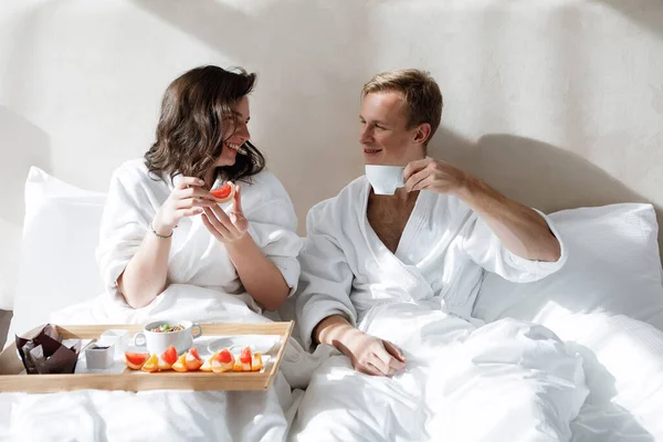 Man and woman have breakfast with a tray of food in bed. Happy couple in a hotel room.