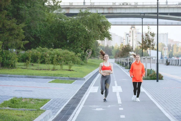 两名身穿运动服的妇女在城市公园的自行车道上跑步 — 图库照片