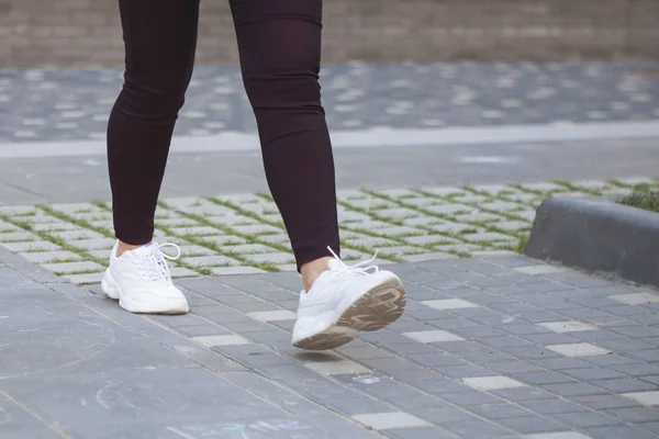 一个穿着白色运动鞋在城市人行道上行走的女孩的腿 — 图库照片