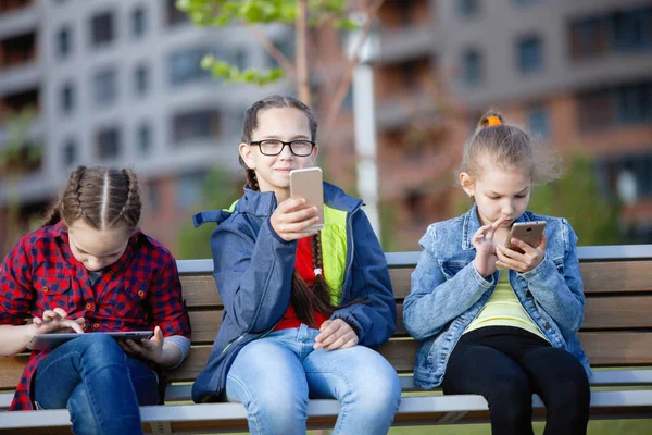 Tres Adolescentes Con Teléfono Inteligente Tableta Sentados Banco Parque Ciudad —  Fotos de Stock