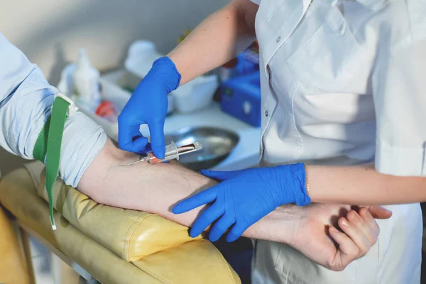 护士做血液检查 戴蓝色乳胶医用手套的女性双手为一名留着胡须的男子注射 肘部戴着眼镜 — 图库照片