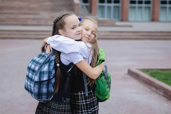 两个身穿校服的女学生相遇站在学校前拥抱 — 图库照片