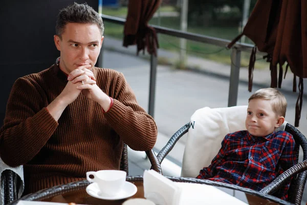 Father and son are sitting at a table in a cafe. Parental love, happy childhood, child care.