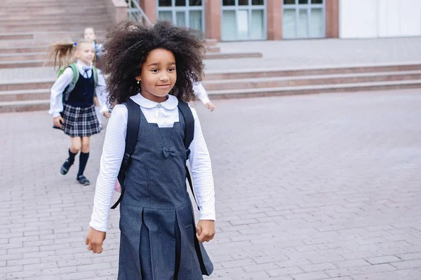 African girl and schoolchildren in uniform joyfully run out the stairs in front of the school.