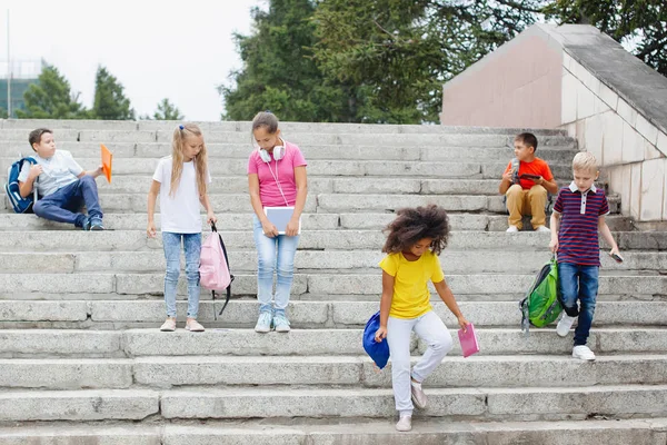 さまざまな国籍の学校の子供たちのグループは カラフルな服の石段の上に座っている 10代の若者が話し ヘッドフォンで音楽を聴き 本を読む — ストック写真