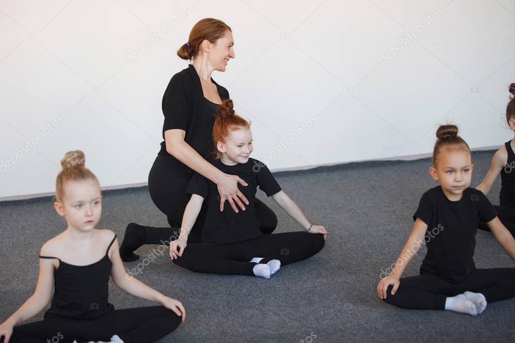 Group of teenage girls dancers in a lesson with a trainer. Black leotard, hair in a bun, white socks.