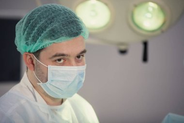 Ameliyat sırasında şapkalı ve maskeli bir doktor..