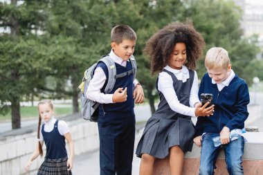 Okul üniformalı üç genç, akıllı bir telefona bakıyorlar. Afrikalı, sarışın ve oğlan