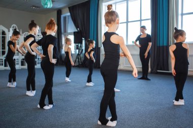 Group of teenage girls in dance, ballet, rhythmic gymnastics classes. Black leotards, hair in a bun, choreography, attentiveness, white socks. Back view. clipart