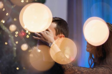 Bir erkek ve bir kadın, süslü bir Noel ağacının yanında birbirlerine sarılıp tebrik ediyorlar..