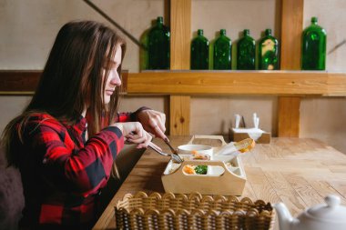 Genç ve güzel bir kadın bir kafede ya da restoranda yemek yiyor.