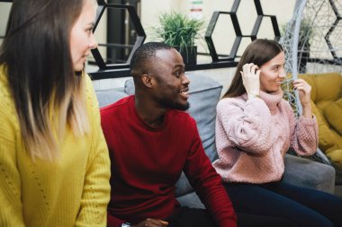 Çok uluslu erkek ve kadınların üç arkadaşından oluşan bir grup bir kafe veya restoranda iletişim kurar, gülümser ve bir masaya güler..