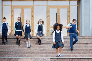 Üniformalı ve sırt çantalı öğrenciler okula gider..