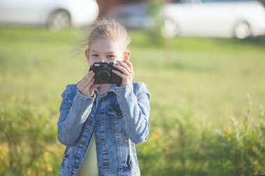 Genç kız şehir parkındaki bir kamerada çekim yapıyor. Mavi ceket ve siyah kot, pembe spor ayakkabı..