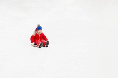 Oğlan beyaz karda bir kalas üzerinde süzülüyor. Şehir parkında güneşli bir kış günü, açık havada..